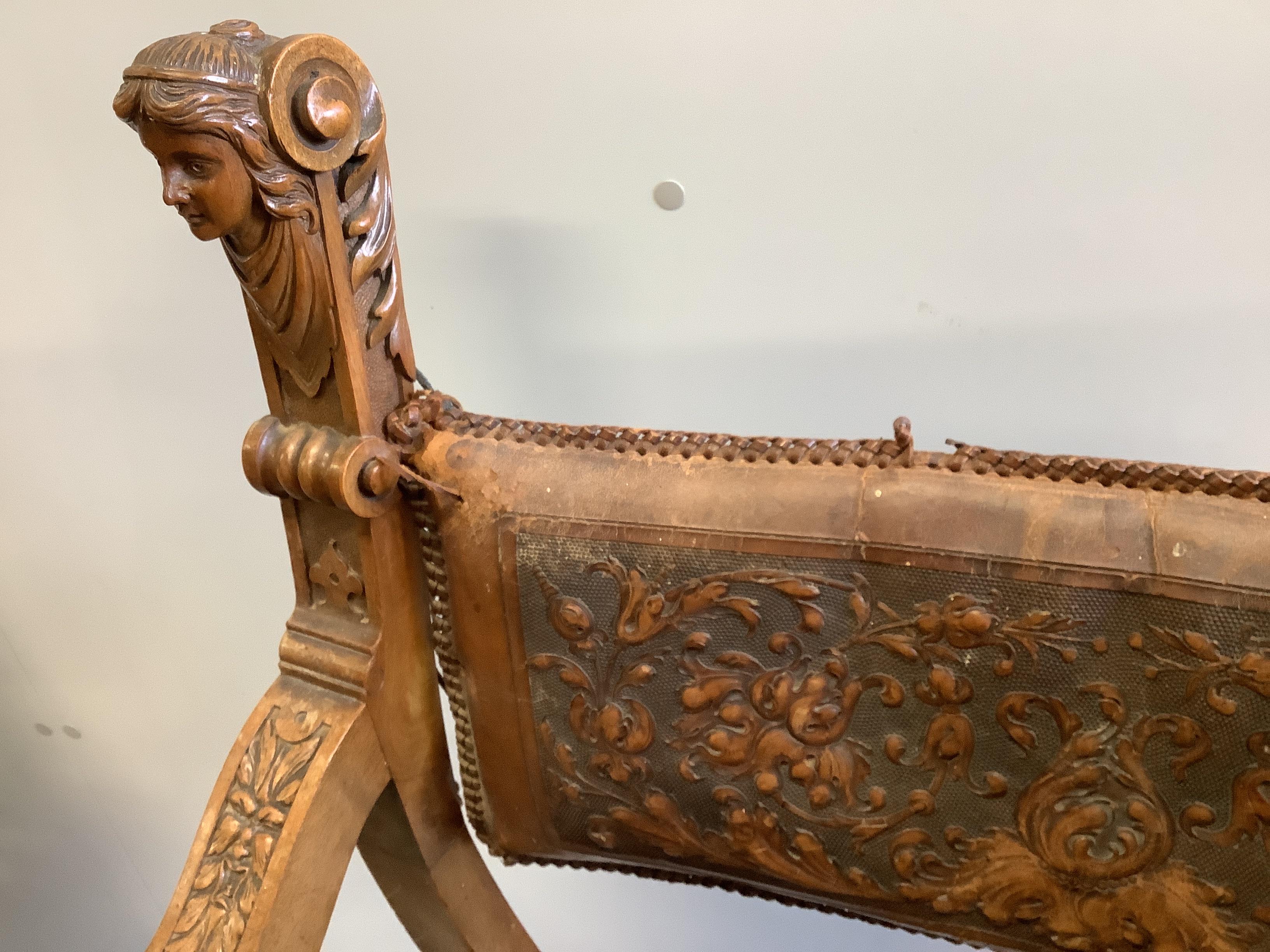 Two continental carved x-framed elbow chairs, each with tooled leather backs and carved terminals, larger width 63cm, depth 66cm, height 100cm